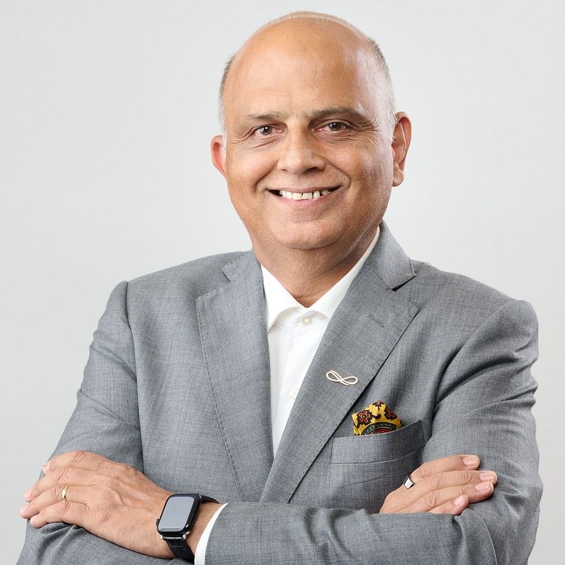 Sanjeev Shekhar in a grey suit and white shirt, standing with arms crossed, smiling slightly against a plain background.