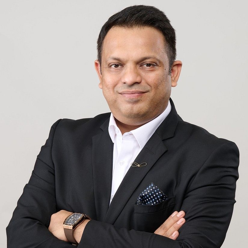 Rahul Singh  in a black suit with a black pocket square, stands with arms crossed, exuding confidence.