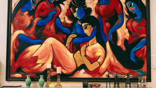 Striking red-toned artwork depicting abstract figures hangs above a vintage wooden console, adding vibrant character to the interiors of Colonel’s Retreat, Defence Colony.