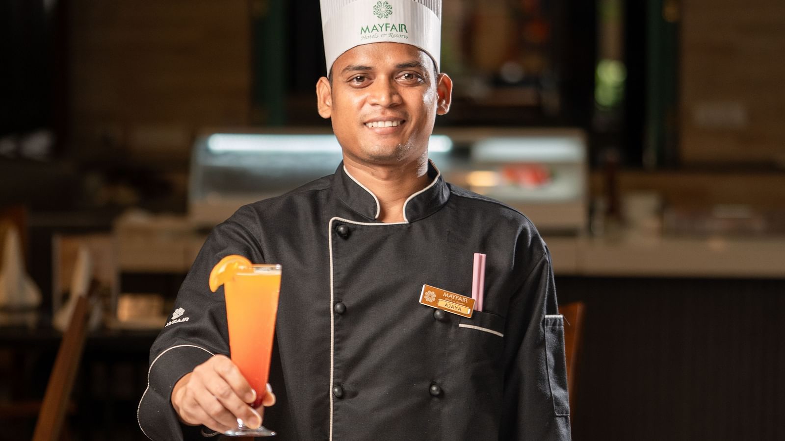 Chef in black uniform holding an orange drink beside plated desserts