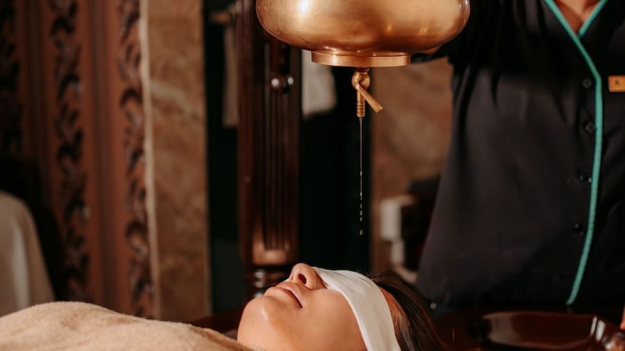 A woman providing an oil relaxation treatment to a guest lying on the bed at Crescent spa & resort, Indore