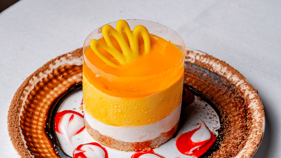 A layered mango cheesecake with a yellow garnish at Café Latte, located within Noor-Us-Sabah Palace, Bhopal, served on a decorative dessert plate.