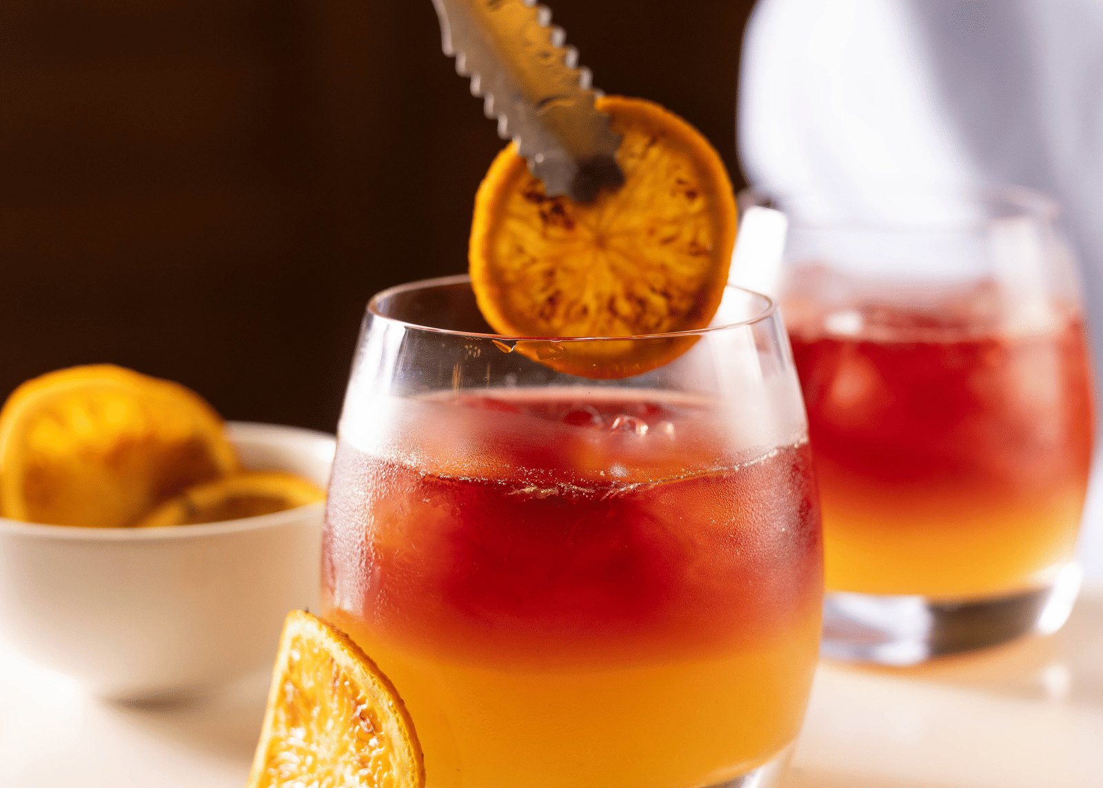 A close-up of a hand stirring a cocktail with orange slices and ice in a glass - Megha Resort & Villas, Dehradun