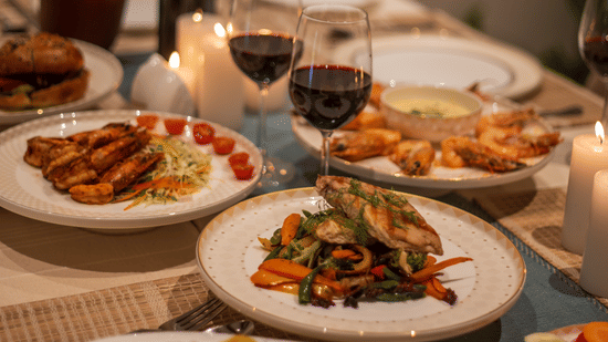 A close-up of a dinner spread with several plates of food, a bottle of wine, and glasses - Lamrin Morjim Goa