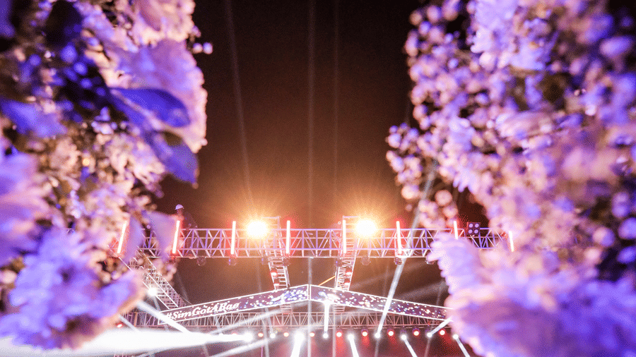 A view down a floral corridor toward a brightly lit performance stage at Ananta Spa & Resort, Jaipur, with one person standing.