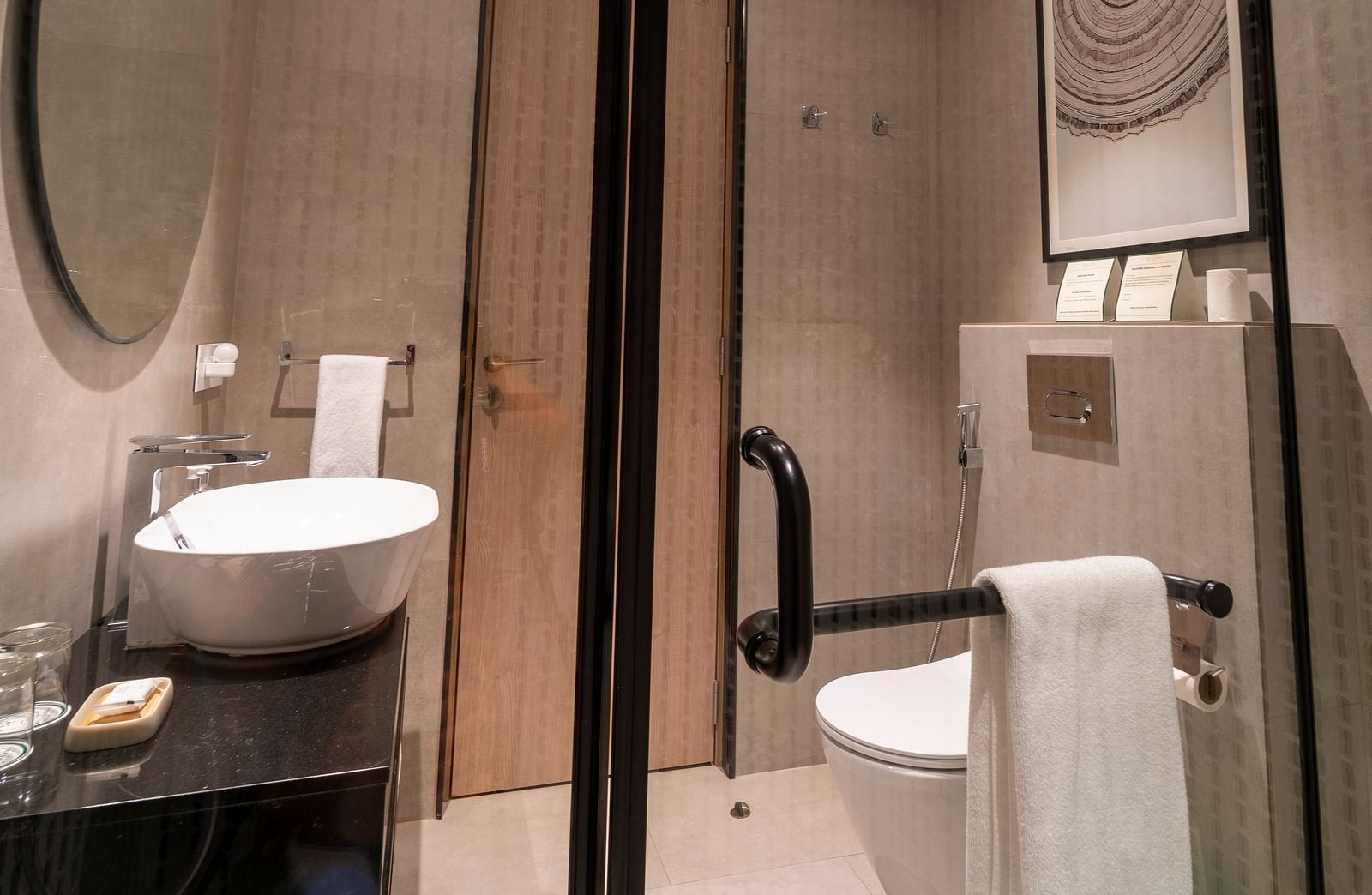 Spacious washroom with glass door partitions, a round wall-mounted mirror above the washbasin, and a western toilet to the side at Nivasana Manali.