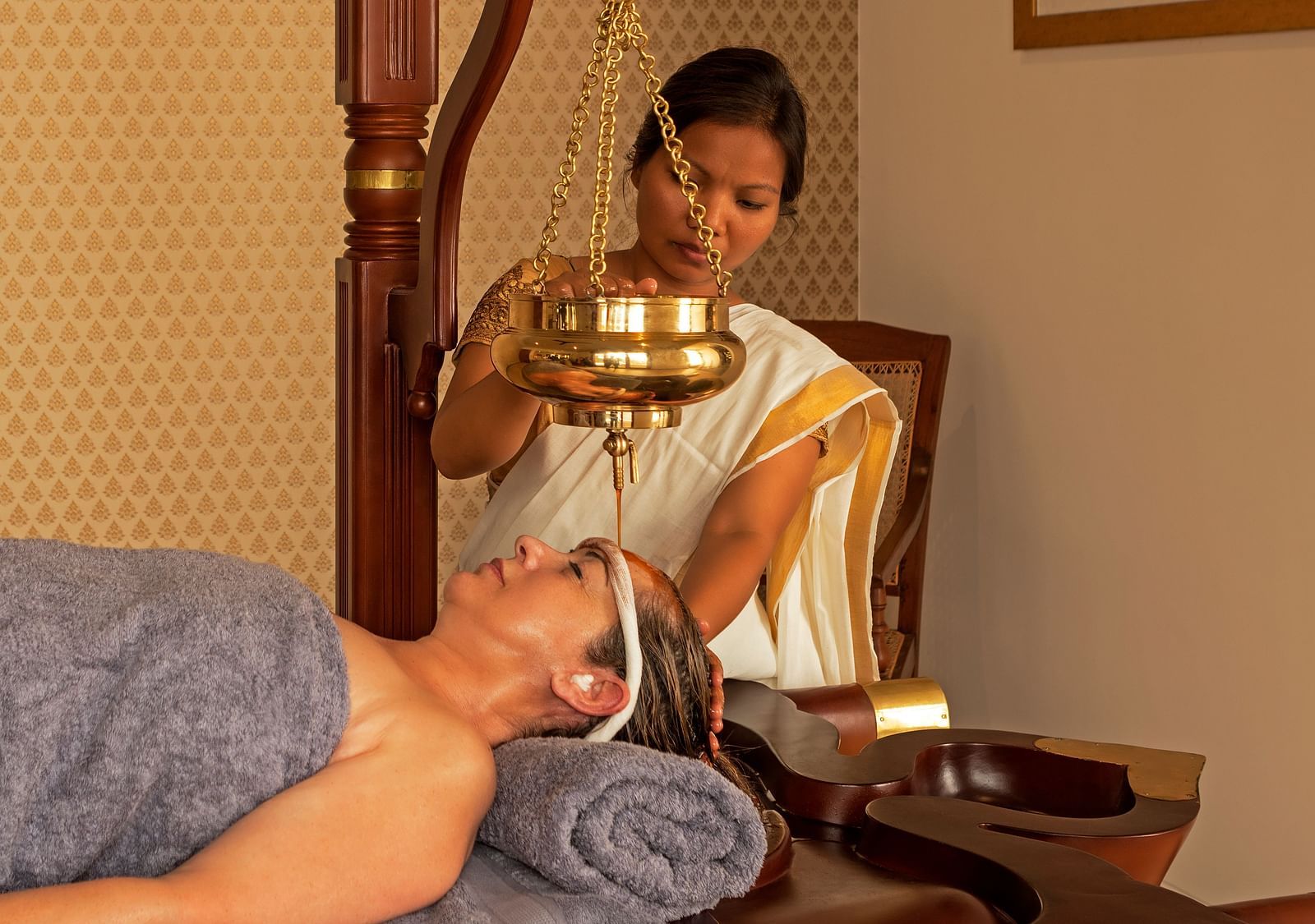 A person receiving a treatment in a room with a painting and wooden furniture - Shreyas Retreat