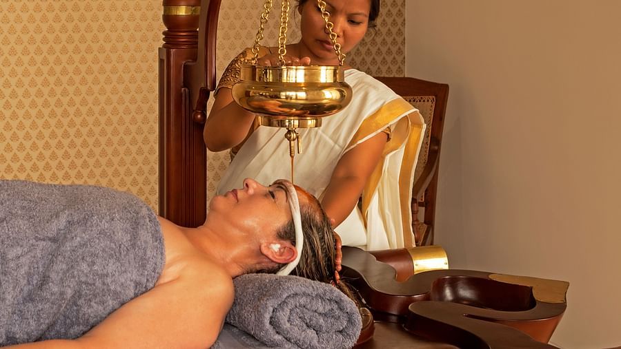 A person receiving a treatment in a room with a painting and wooden furniture - Shreyas Retreat