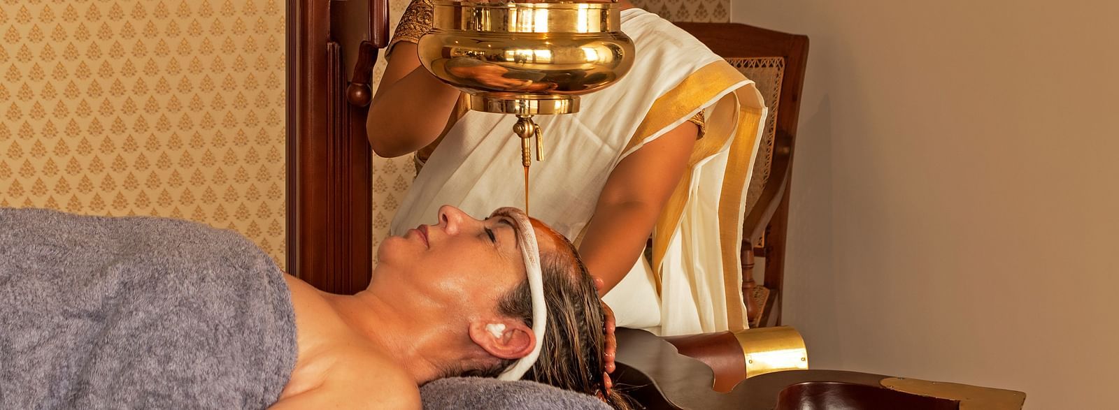 A person receiving a treatment in a room with a painting and wooden furniture - Shreyas Retreat