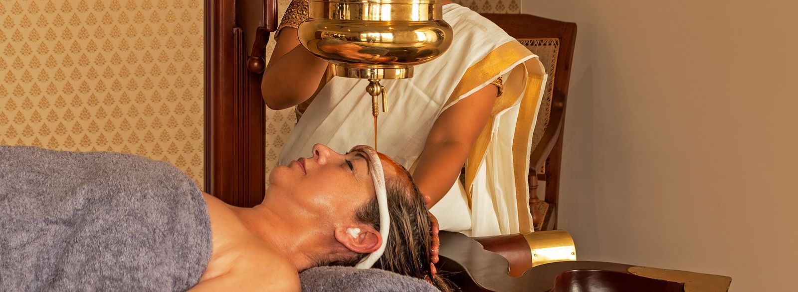 A person receiving a treatment in a room with a painting and wooden furniture - Shreyas Retreat