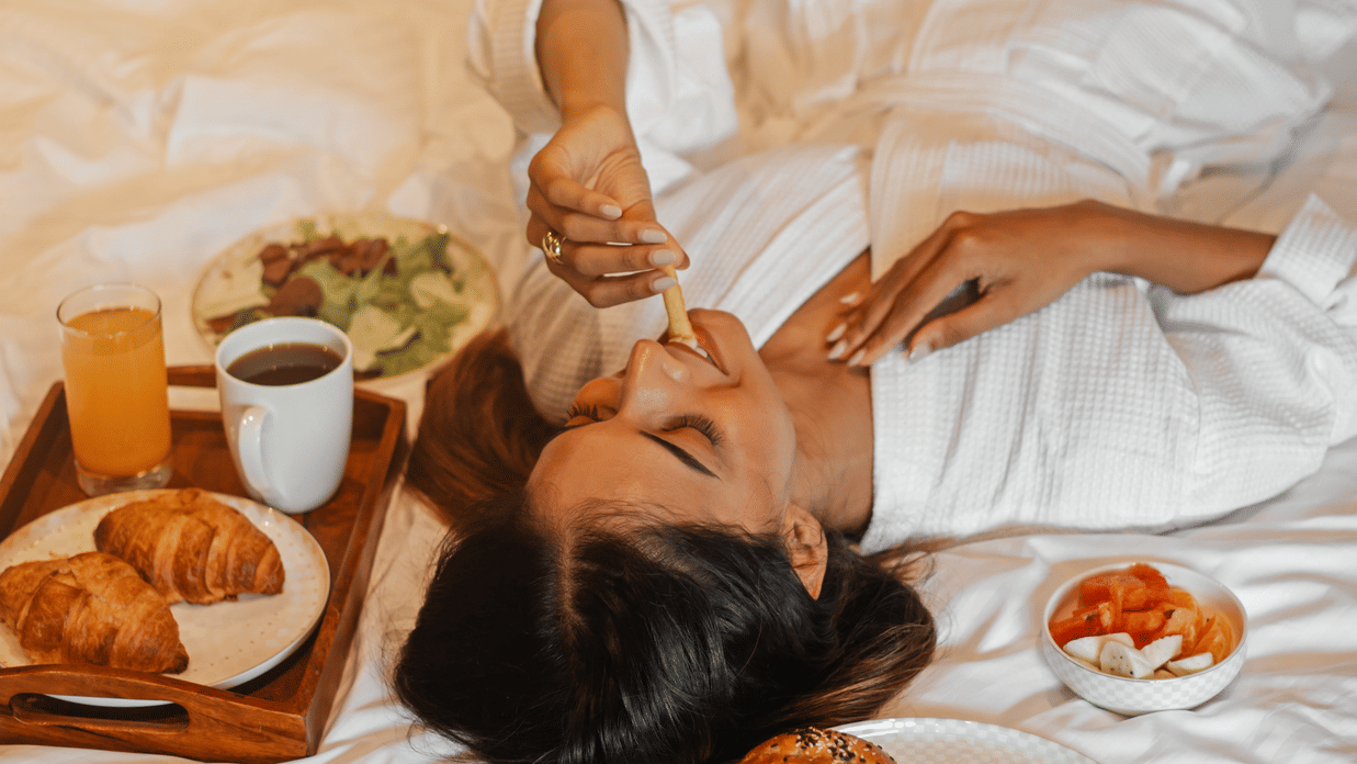 A woman having breakfast in bed with pastries and coffee kept nearby - Lamrin Morjim Goa