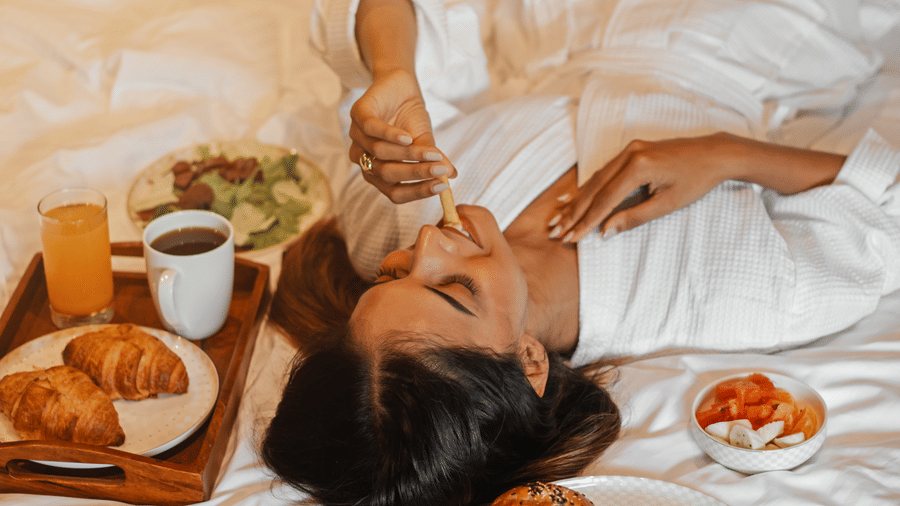 A woman having breakfast in bed with pastries and coffee kept nearby - Lamrin Morjim Goa