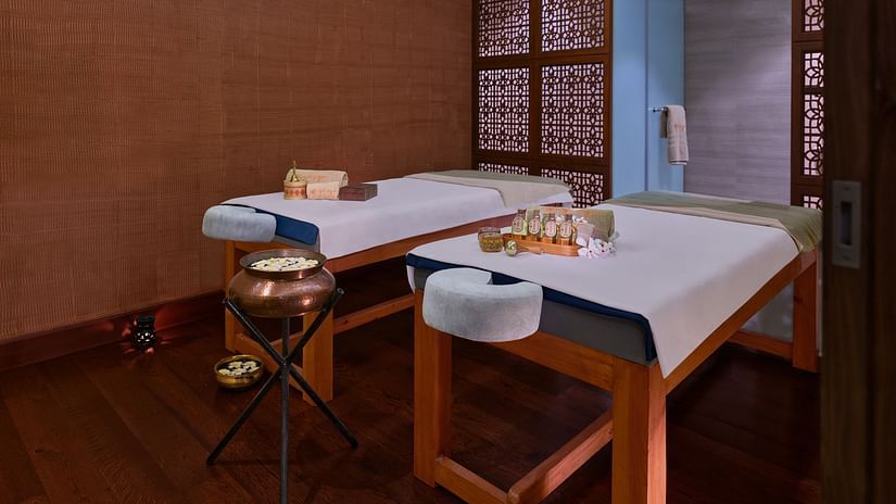 Two massage tables in a dimly lit spa room with various treatment products - The Resort, Mumbai.