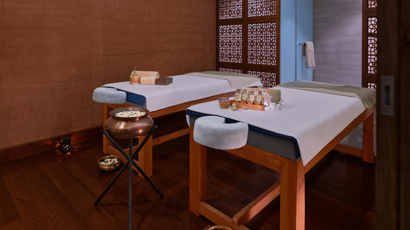 2 massage tables in a dimly lit spa room with various treatment products | The Resort, Mumbai.