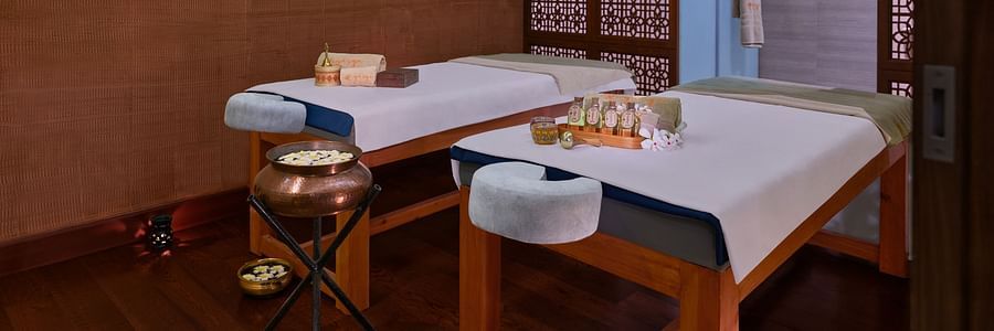 Two massage tables in a dimly lit spa room with various treatment products - The Resort, Mumbai