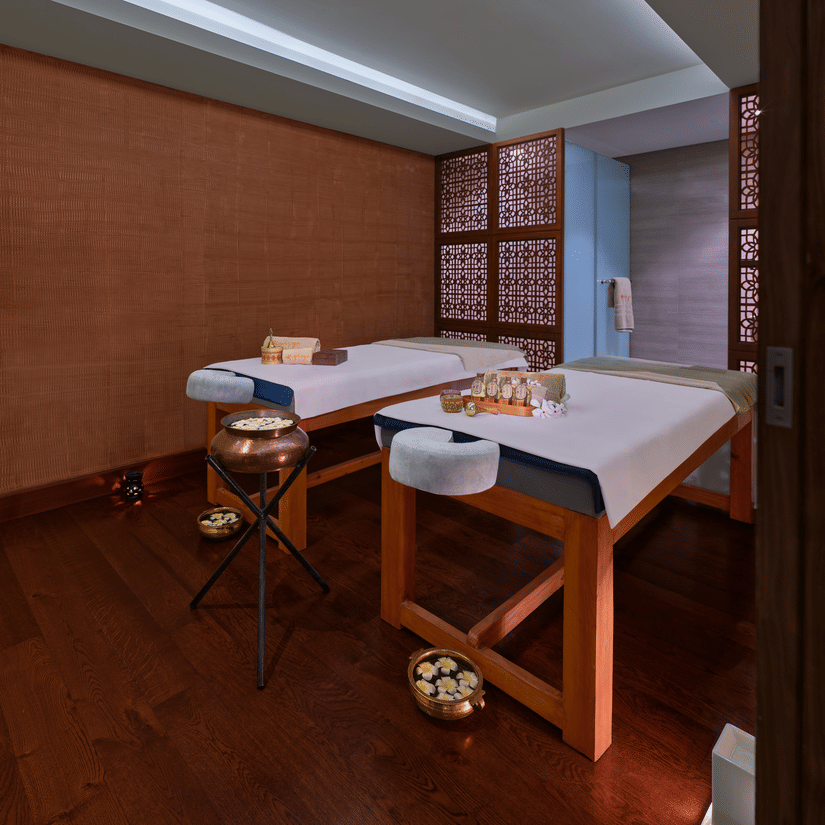 2 massage tables in a dimly lit spa room with various treatment products | The Resort, Mumbai.