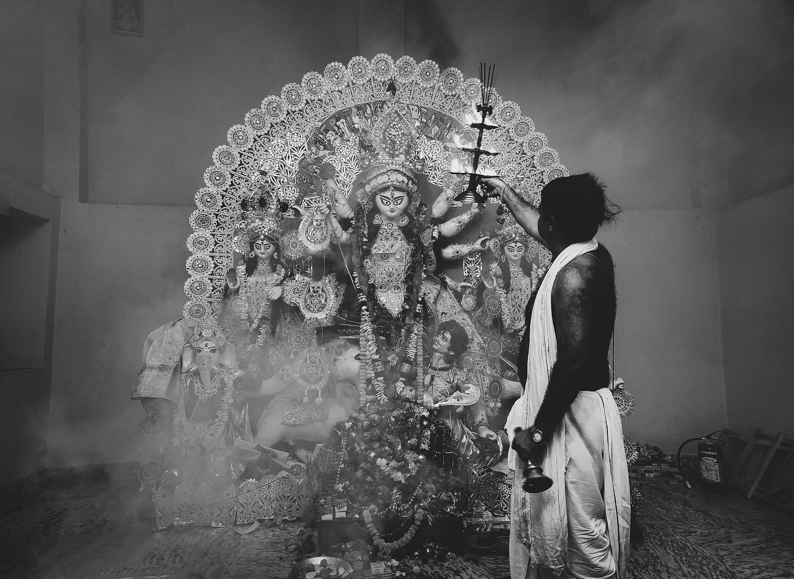 Priest performing aarti before a beautifully decorated Durga idol in a smoke-filled atmosphere.