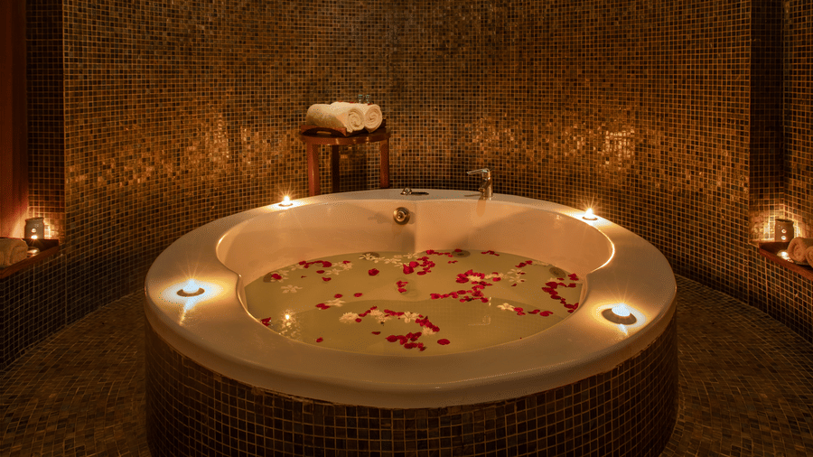 Circular spa Jacuzzi filled with rose petals and warm candlelight at Kenilworth Resort & Spa, Goa.