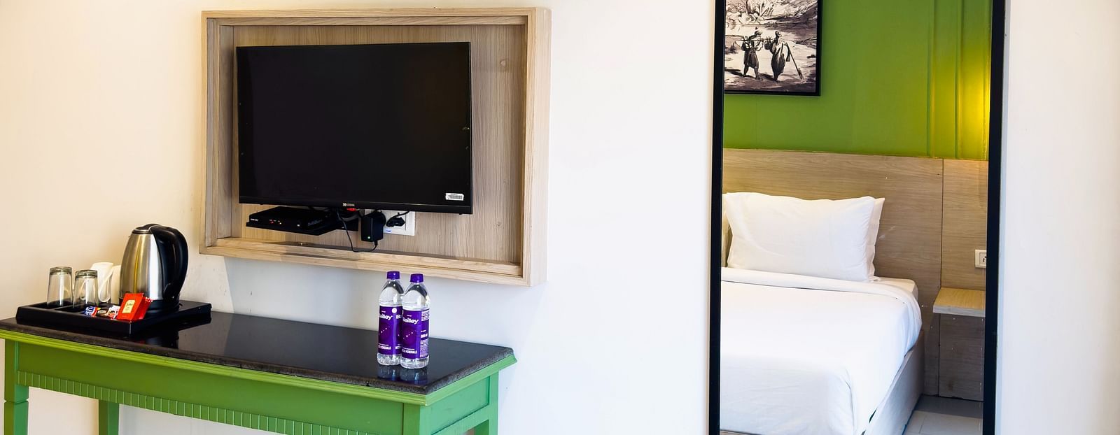 A hotel room with a wall-mounted television near a mirror showing the reflection of the bed - Wonder Hills