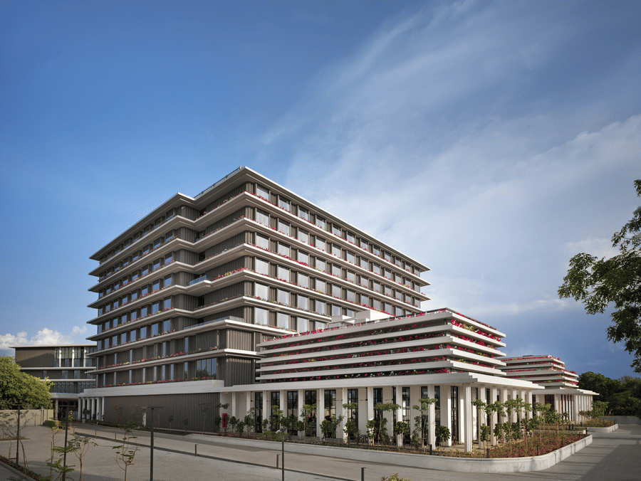 Daytime exterior view of The Residency Signature Madurai with a modern multi-storey facade, manicured grounds, and a bright blue sky.