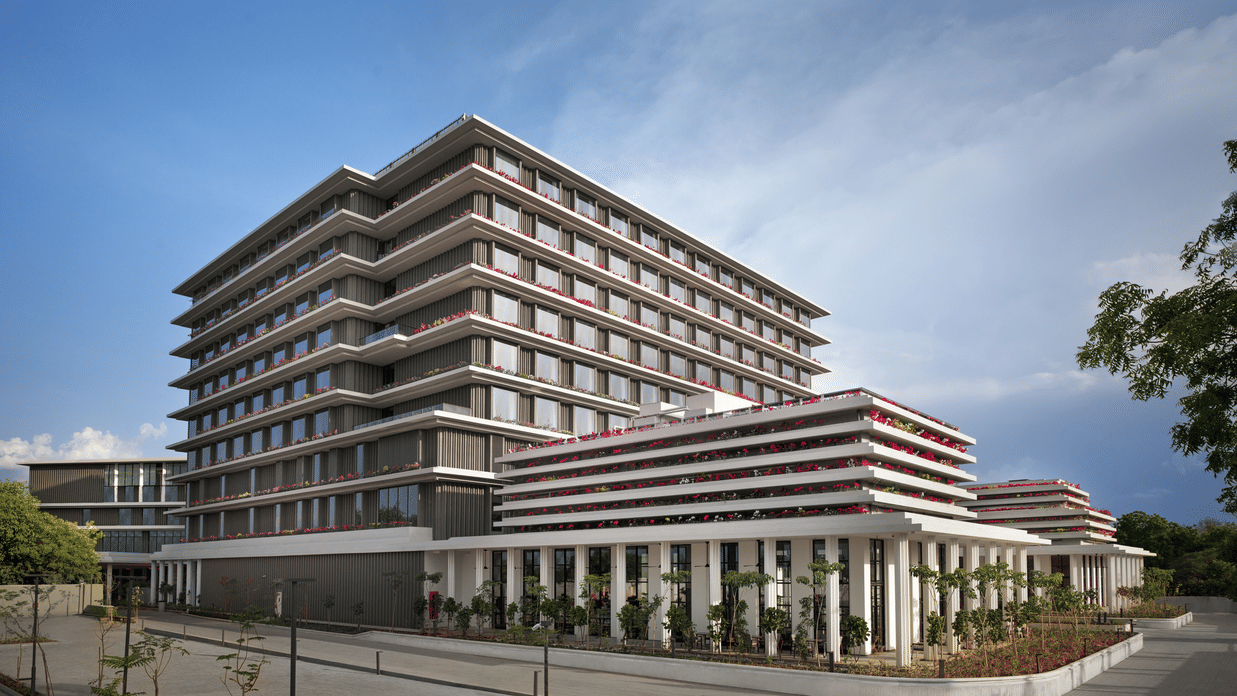 Daytime exterior view of The Residency Signature Madurai with a modern multi-storey facade, manicured grounds, and a bright blue sky.