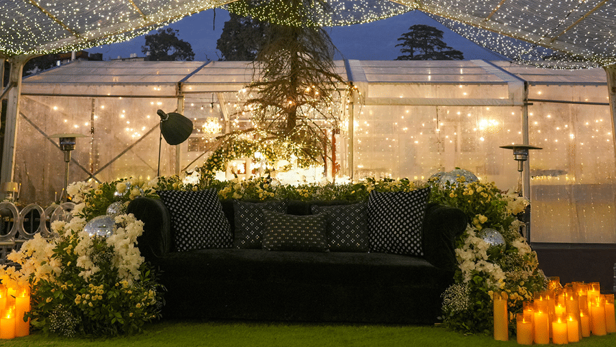 An outdoor event space featuring a dark couch backdrop illuminated with string lights under a tent canopy at Ramada by Wyndham Mussoorie Mall Road.