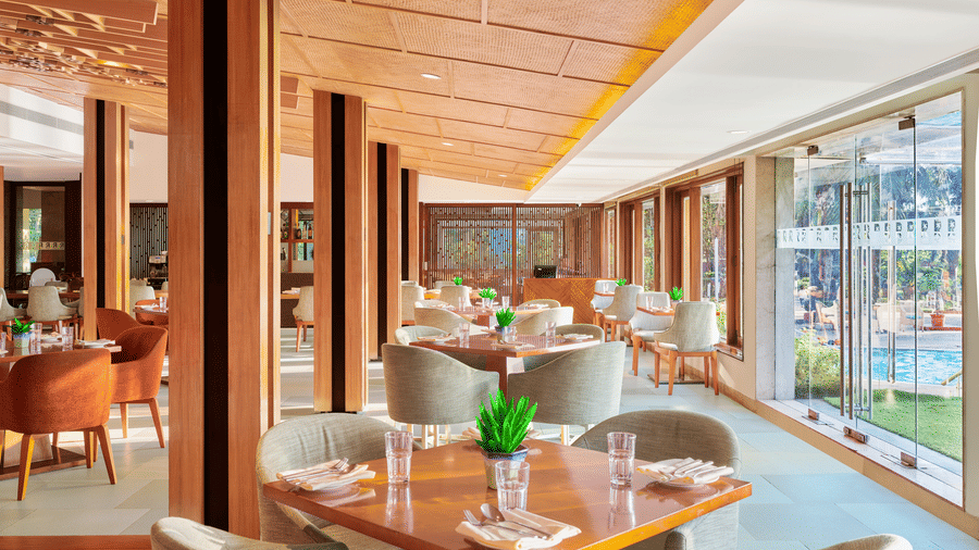 Chairs and tables placed right beside a glass window in High Tide, our sea-view restaurant inside The Resort, Mumbai, one of the ideal anniversary places in Mumbai