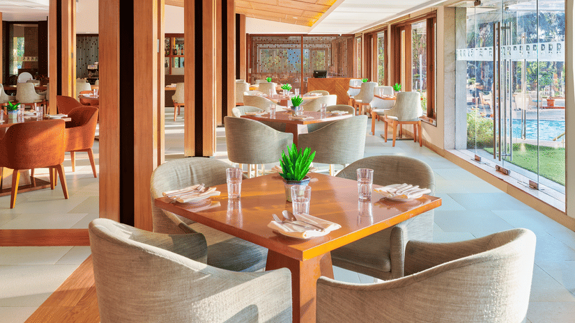 Chairs and tables placed right beside a glass window in High Tide, our sea-view restaurant inside The Resort, Mumbai, one of the ideal anniversary places in Mumbai