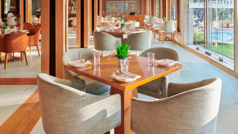 Chairs and tables placed right beside a glass window in High Tide, our sea-view restaurant inside The Resort, Mumbai, one of the ideal anniversary places in Mumbai