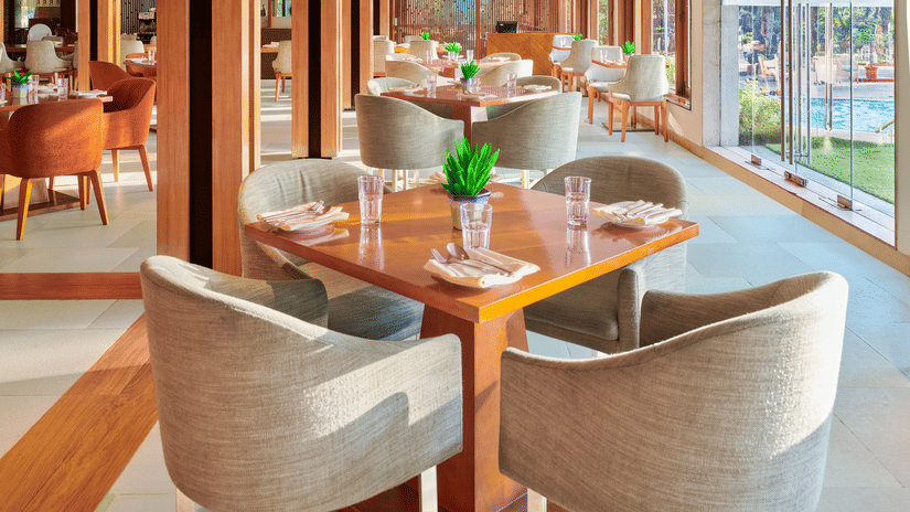 Chairs and tables placed right beside a glass window in High Tide, our sea-view restaurant inside The Resort, Mumbai, one of the ideal anniversary places in Mumbai