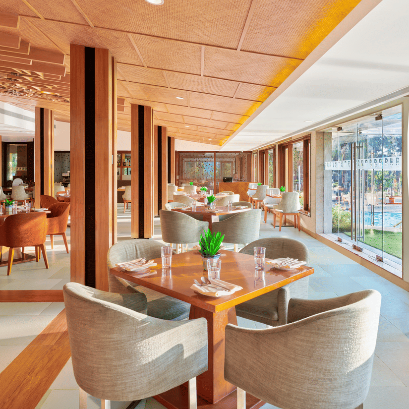 Chairs and tables placed right beside a glass window in High Tide, our sea-view restaurant inside The Resort, Mumbai, one of the ideal anniversary places in Mumbai