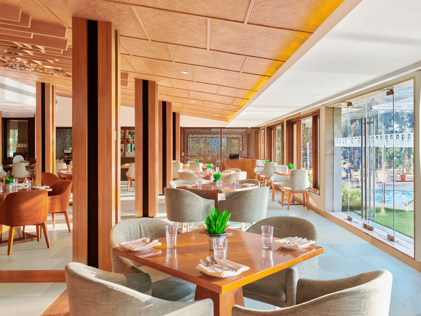 Chairs and tables placed right beside a glass window in High Tide, our sea-view restaurant inside The Resort, Mumbai, one of the ideal anniversary places in Mumbai