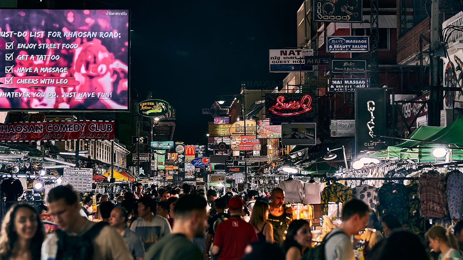 People walking in Khao San Road with shops on either side and ad boards above