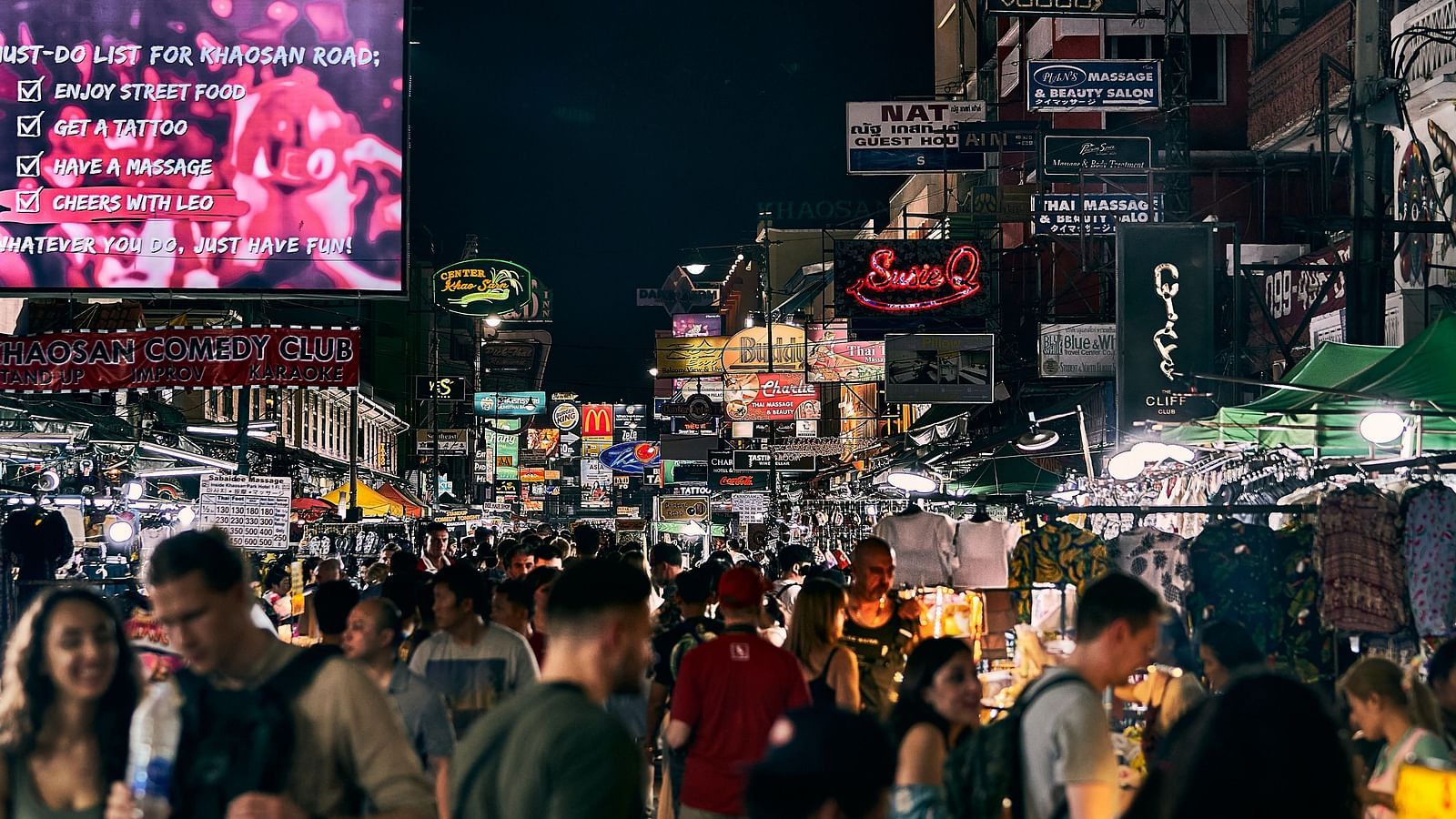 People walking in Khao San Road with shops on either side and ad boards above
