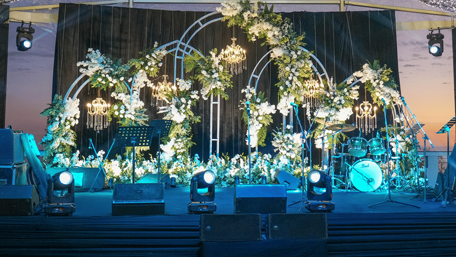 An illuminated event stage, decorated with floral arches and lighting arrangements under a tent ceiling at Ramada by Wyndham Mussoorie Mall Road.