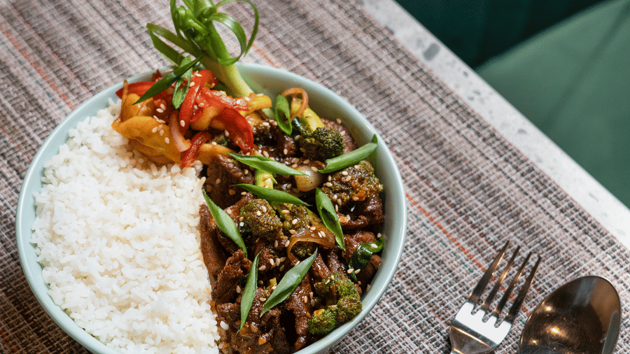 A ceramic bowl of white rice topped with a dark, savoury vegetable stir-fry and garnished with fresh green spring onions at Apartel by Aarin, Oragadam.