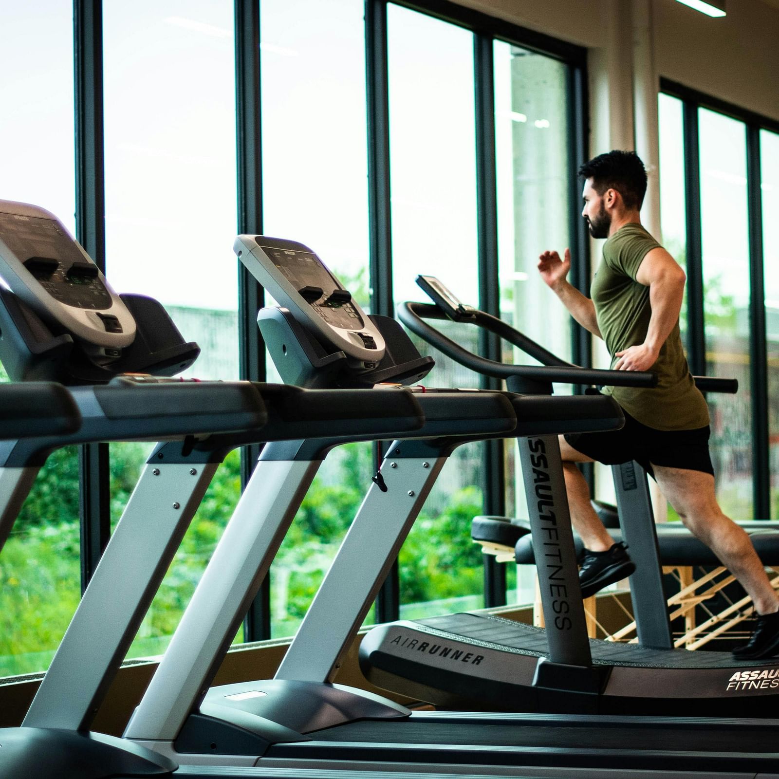 image of a man running on a treadmill in a gym with glass panels opening to green surroundings