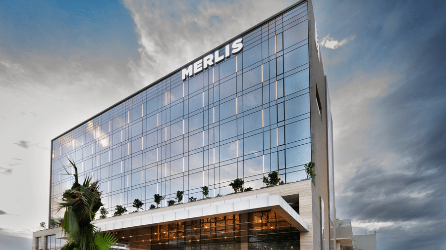 Facade view of Merlis Hotel in Coimbatore, featuring a modern glass-fronted exterior, illuminated entrance, and a car parked at the driveway.