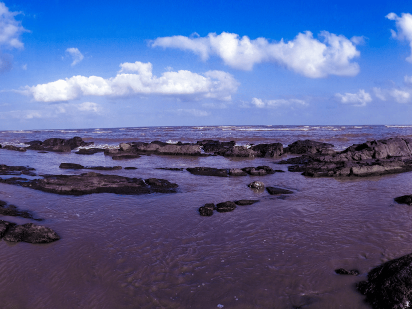 Rocky shoreline at Daman Beach featuring tidal pools, coastal rock formations, and sweeping sea views under a dramatic sky