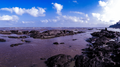 Rocky shoreline at Daman Beach featuring tidal pools, coastal rock formations, and sweeping sea views under a dramatic sky