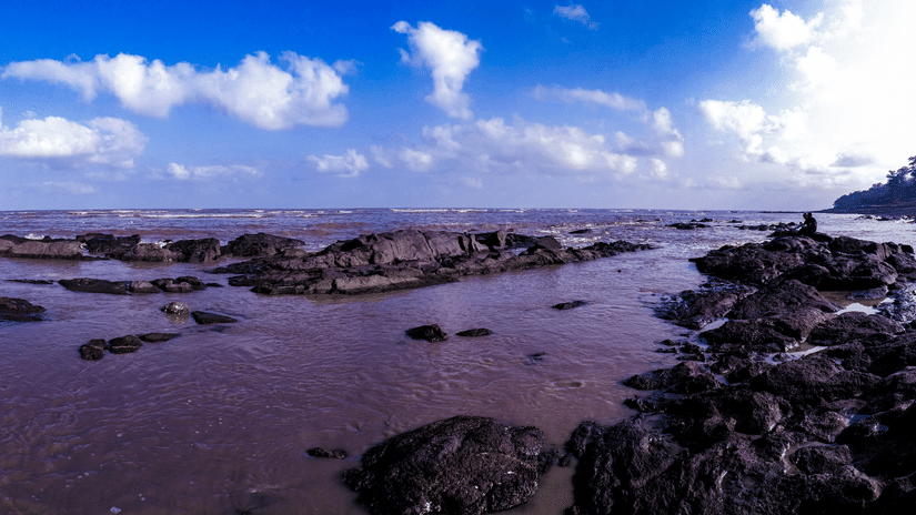 Rocky shoreline at Daman Beach featuring tidal pools, coastal rock formations, and sweeping sea views under a dramatic sky