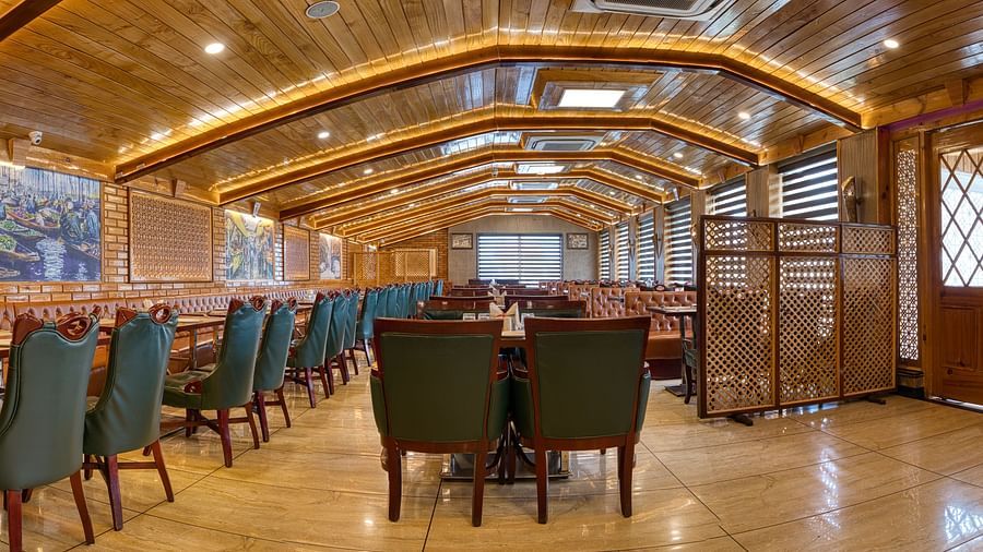 Wide-angle view of the elegant restaurant at Royal Comfort Regency, featuring long tables and a stylish wooden ceiling design.