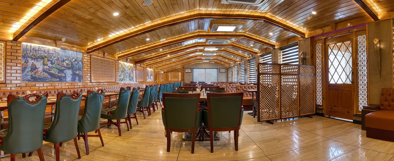 Wide-angle view of the elegant restaurant at Royal Comfort Regency, featuring long tables and a stylish wooden ceiling design.