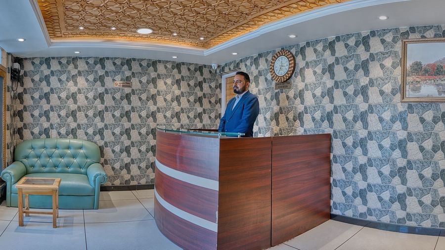 The reception desk at Royal Comfort Regency with a patterned feature wall, green sofa seating and a staff member attending guests.