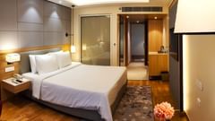 A bright, contemporary Executive Room at Golden Sarovar Portico, Amritsar, showing a king-sized bed with crisp white linens, a dark, plush headboard, and stylish, modern lighting fixtures.