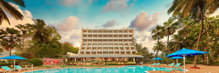 A long shot of the facade of The Resort, Mumbai (One of the best Beach Resorts Near Mumbai for a Family), with a pool in the foreground - Romantic Getaway in Mumbai