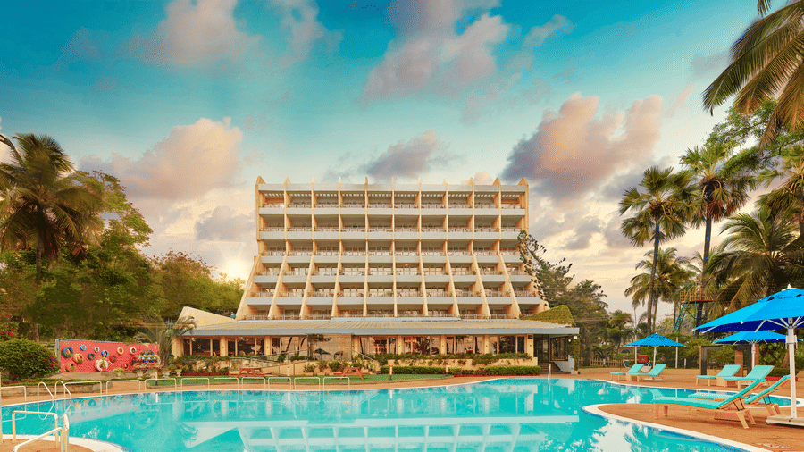 A long shot of the facade of The Resort, Mumbai (One of the best Beach Resorts Near Mumbai for a Family), with a pool in the foreground - Romantic Getaway in Mumbai