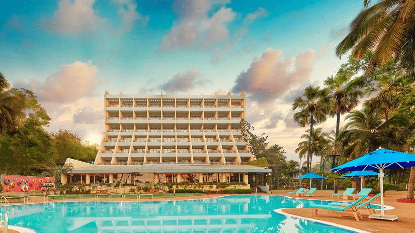 A long shot of the facade of The Resort, Mumbai (One of the best Beach Resorts Near Mumbai for a Family), with a pool in the foreground - Romantic Getaway in Mumbai
