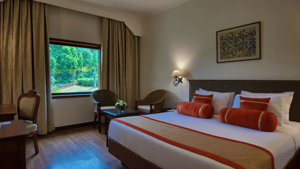The Deluxe King Garden View bedroom at Clarks Khajuraho with a large bed, side tables with lamps, a television unit, and curtains framing a window.