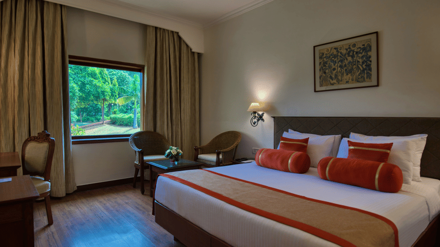 The Deluxe King Garden View bedroom at Clarks Khajuraho with a large bed, side tables with lamps, a television unit, and curtains framing a window.